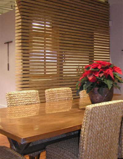 Wooden dining table with woven chairs and a potted poinsettia in a modern room with slatted wooden wall panel.