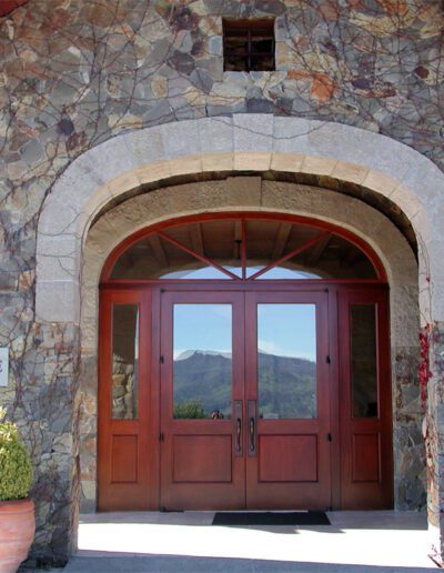 Stone facade of a winery entrance with wooden double doors and signs displaying "cardinale" and "open daily.