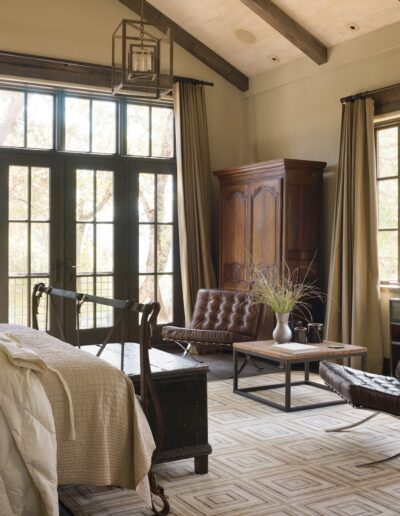 A cozy bedroom with a classic design featuring a leather sofa, wooden furniture, and french doors leading outside.
