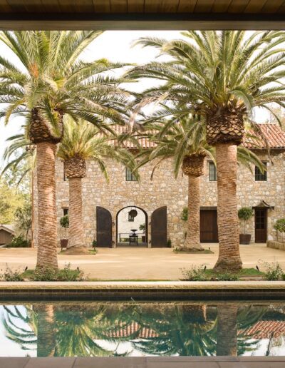 Stone villa with palm trees viewed from a poolside perspective.