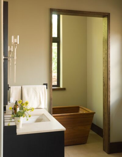 A modern bathroom with a wooden bathtub and a white sink on a black countertop, accented by yellow flowers.
