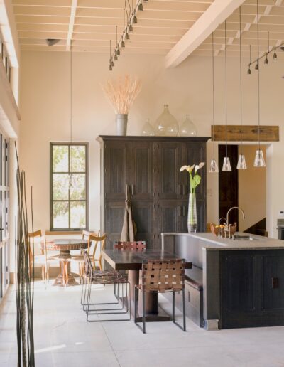 Modern rustic kitchen with a large dark wood cabinet, a central island, pendant lighting, and a dining area with natural light.