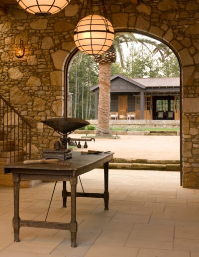 Stone archway framing a view of a rustic patio, with an antique table in the foreground inside an elegant room.