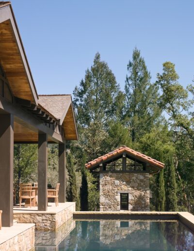 Luxurious poolside area of a modern house with stone accents and a forest backdrop.