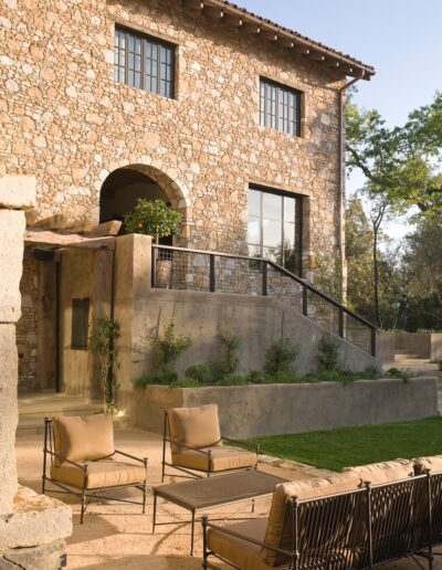 Stone house exterior with patio seating and staircase leading to a balcony.