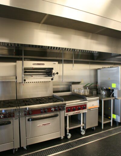 A professional stainless steel kitchen with cooking ranges, ovens, and prep stations.