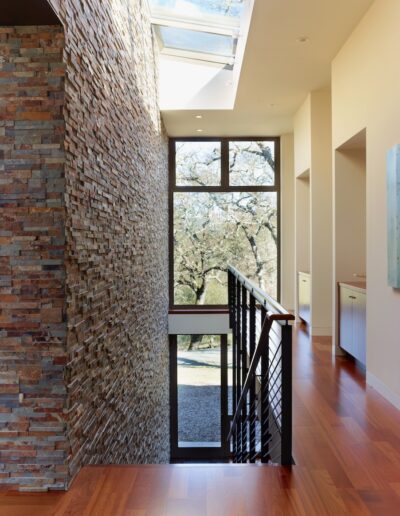 Modern hallway with brick wall, wooden flooring, and large window overlooking trees.