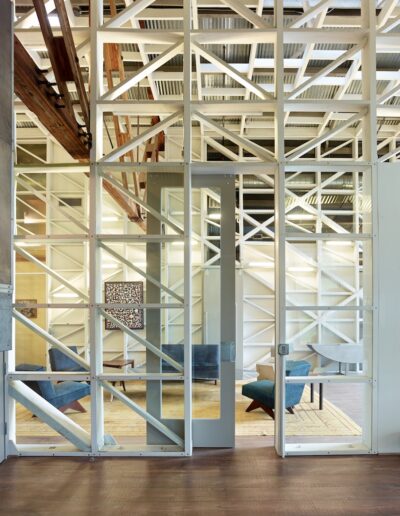Modern office space with a glass and metal partition, featuring exposed wooden beams and a cozy seating area.