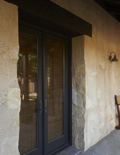 A rustic building entrance featuring stone walls and a wooden rocking chair by the door.