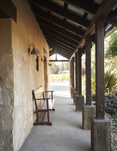 A peaceful corridor with a wooden rocking chair, featuring rustic pillars and a vineyard in the background.