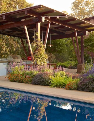 A tranquil backyard scene featuring a swimming pool, a covered patio area with outdoor seating, and lush landscaping bathed in warm, evening light.