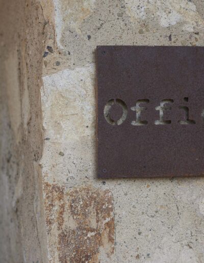 Rustic metal "offices" sign mounted on a textured stone wall.