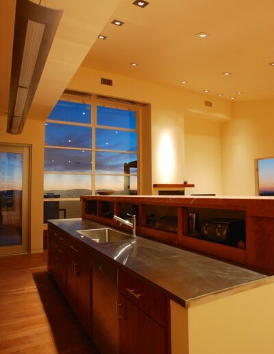 Modern kitchen interior at dusk with stainless steel appliances and ample recessed lighting.