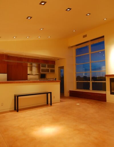 Spacious modern living room with an open kitchen layout, large windows, and recessed lighting at dusk.