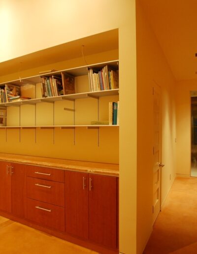 A warm-lit room featuring a built-in bookshelf and cabinet unit with a wooden door at the far end.