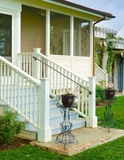 A well-maintained porch with white railings and steps leading up to a house with a large window and green lawn.