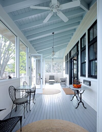 Spacious covered porch with blue ceiling, wicker chairs, and elegant black framed windows.