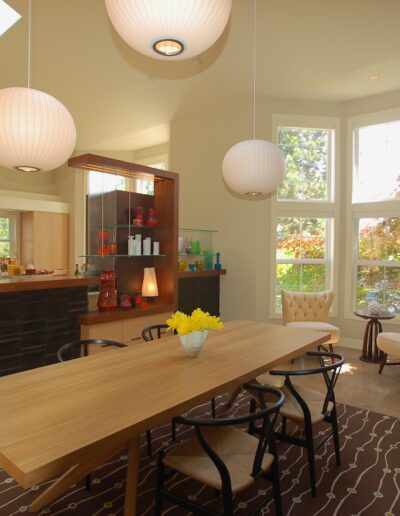 Bright, modern kitchen with wooden dining table, pendant lighting, and a view of the outside through large windows.