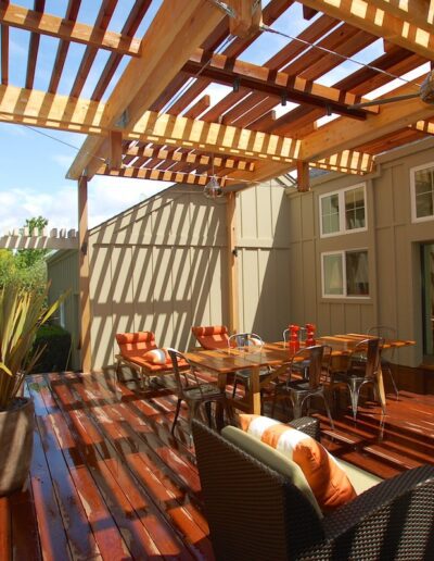 Sunny wooden deck with pergola, outdoor seating, and potted plants.