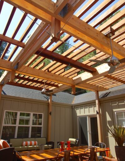 Wooden pergola over a patio dining area with furniture and hanging lights.