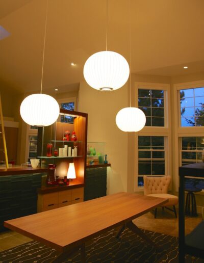 Modern dining room with three pendant lights and large windows at dusk.