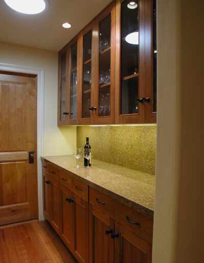 A well-lit, traditional kitchenette with wooden cabinets, granite countertop, and a wine bottle with glasses.